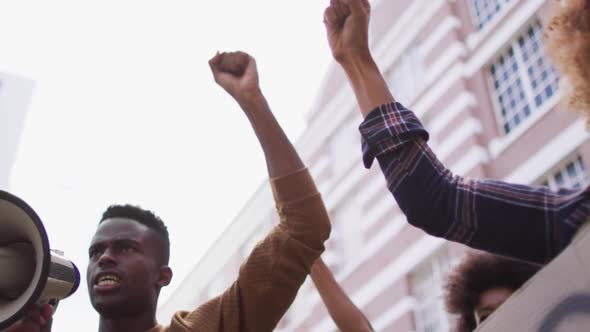 African american man shouting using megaphone with other people raising fists during protest