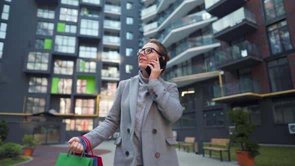 Woman Walking on a Business District with Shopping Bags and Talking on the Smartphone