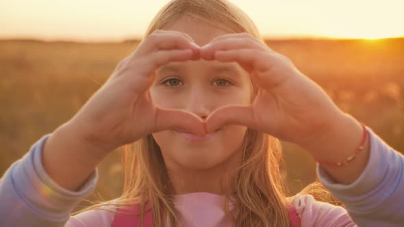 Little Girl Makes a Heart with Her Hands at Sunset.