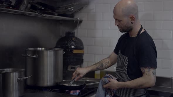 Side View of Male Chef in Apron Flambeing Food in Restaurant Kitchen