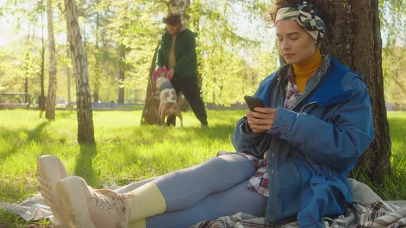 Woman Sitting in Park and Using Smartphone