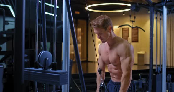 Handsome Young Male Athlete Doing Exercises on a Strength Trainer Pulling a Rope with Weights