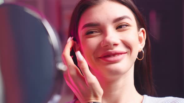 Beautiful Girl with Perfect Skin Face Looks Herself in Mirror in Beauty Salon