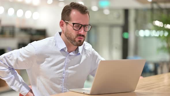 Hardworking Businessman with Laptop Having Back Pain in Office 