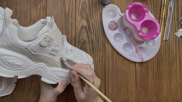 Top View of Hands Paint White Boots with Brush on Desktop