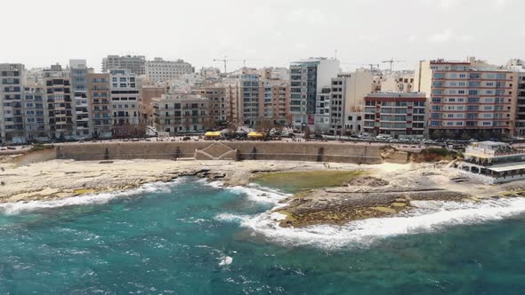Pull back aerial reveal of the resort town of Sliema as seen from the coast of the Mediterranean sea