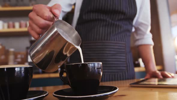 Waiter pouring milk in coffee cup while preparing coffee