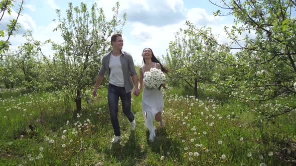 Happy Couple Running Holding Hands in Fruit Garden