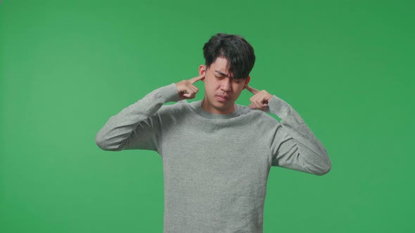 Stressed Asian Man Covering Her Ears While Standing In Front Of Green Screen Background