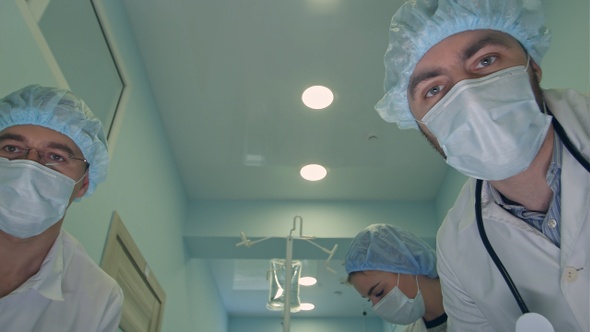 Group of surgeons looking down at patient on the way to operation room