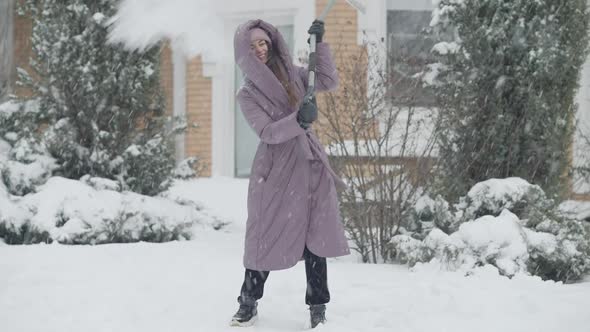 Joyful Slim Charming Woman Cleaning Snow with Shovel and Spinning Laughing Outdoors