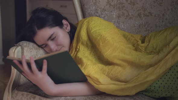 Portrait of a Girl Reading a Book Lying on the Couch