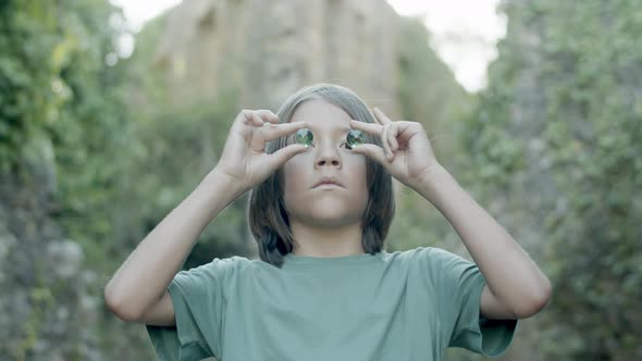 Serious Caucasian Boy Standing and Putting Pebbles on His Eyes