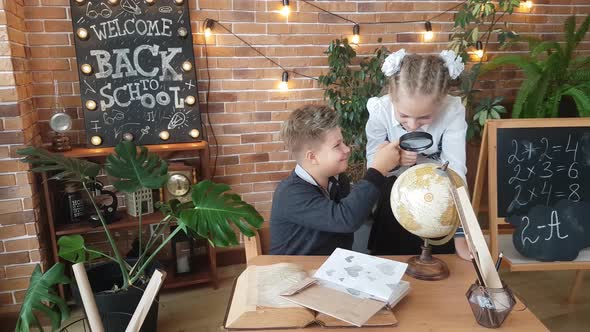 Schoolchildren - a boy and a girl are studying the globe with a magnifying glass