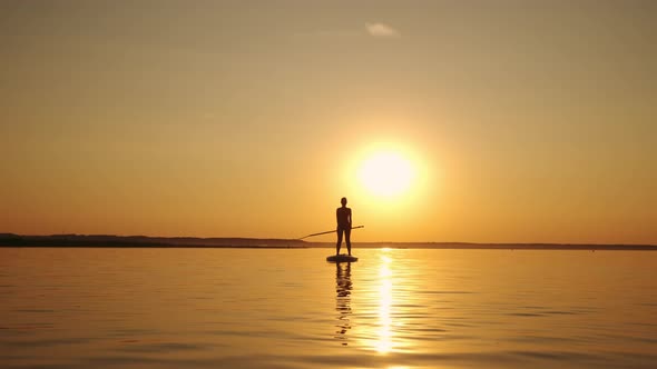 Wide Shot of Siluet of Woman Standing Firmly on Inflatable SUP Board and Paddling Through Shining