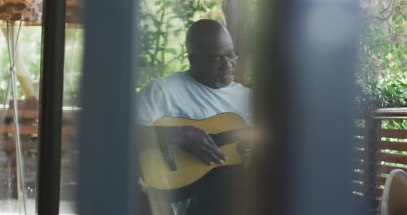 Thoughtful african american senior man sitting on balcony playing acoustic guitar