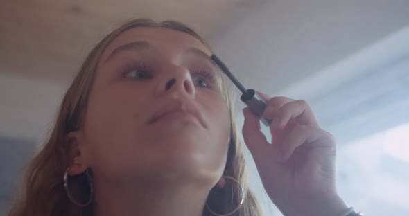 Reflection in the Mirror of a Beautiful Young Woman Putting On Makeup