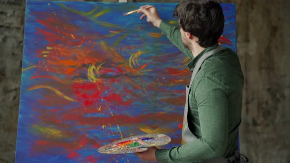 Inspired Male Artist Puts the Finishing Touches to His Painting in a Bright Studio