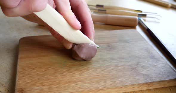 An artist cutting and sculpting soft brown modeling clay with a wood hand tool  while creating a pro