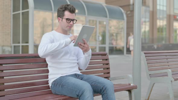 Young Man Using Tablet While Sitting Outdoor on Bench