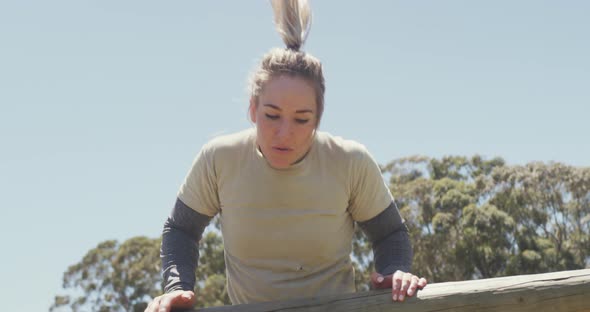 Fit caucasian female soldier going over and under hurdles on army obstacle course in the sun