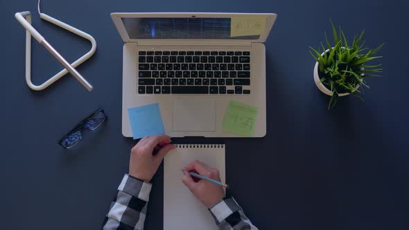 Girl in a Gray Shirt Sitting at the Table Depicts Time and Money on a Notepad. Overhead Shot