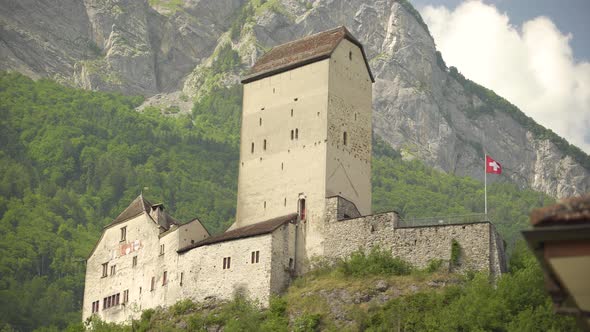 Low angle of historical Sargans Castle with Swiss flag waving on a hill near Mount Gonzen surrounded