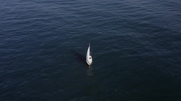 Sail boat sailing slowly towards a setting Sun in the Mediterranean Sea.