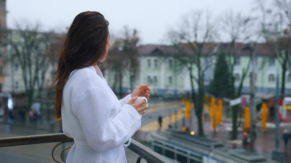 Photo of a beautiful girl in a bathrobe on the hotel balcony with a cup of coffee.