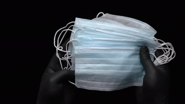 Anonymous paramedic hands showing lot medical face masks, holding equipment on black background