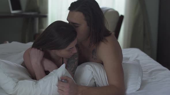 Handsome Man Cuddles His Girl Lying in Bed and Kissing Her Tenderly Close Up