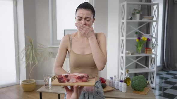 Portrait of Young Beautiful Vegan Woman Standing Indoors As Hand Showing Raw Meat