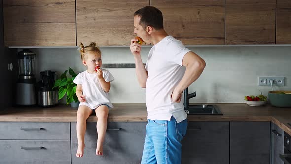 Cute Little Girl and Her Handsome Dad are Eating Fruit in Modern Kitchen