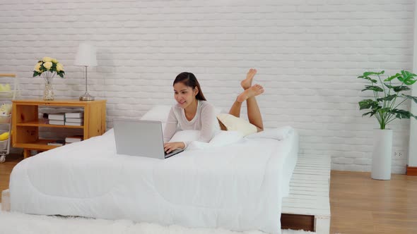 Asian young woman lying on bed and using computer laptop for using social media and shopping online