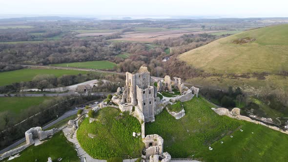 Corfe Castle ruins on green hill at dusk, England. Aerial drone orbiting