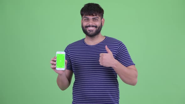 Happy Young Overweight Bearded Indian Man Showing Phone and Giving Thumbs Up