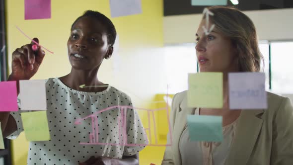 Two diverse female colleagues making notes and discussing at work