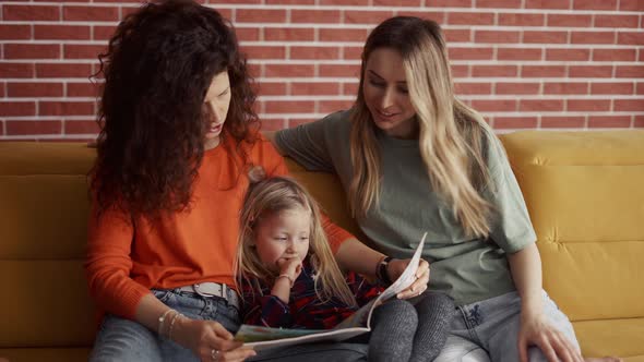 Close Up of Young Women Read a Book Together to a Small Preschool Girl on Sofa