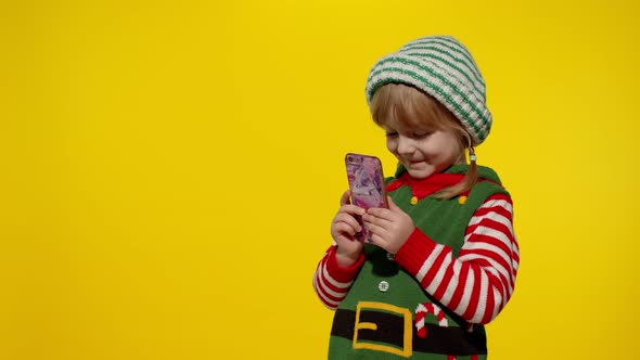 Kid Girl Mobile Phone Christmas Elf Santa Helper Costume Points Fingers Aside Blank Wall