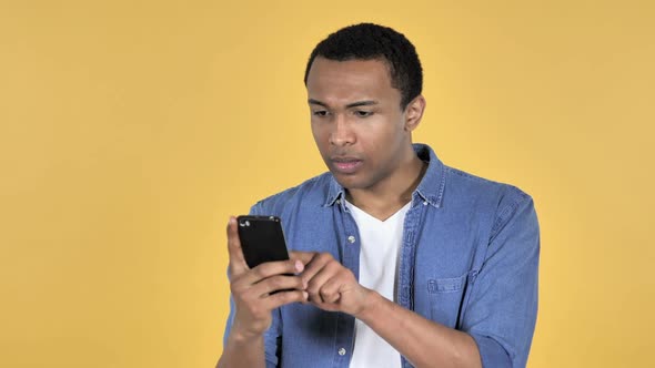 Young African Man in Shock While Using Smartphone Yellow Background