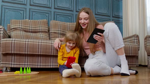 Mother and Daughter Child Sit on Floor at Home Working on Mobile Phone and Tablet Watching Cartoon