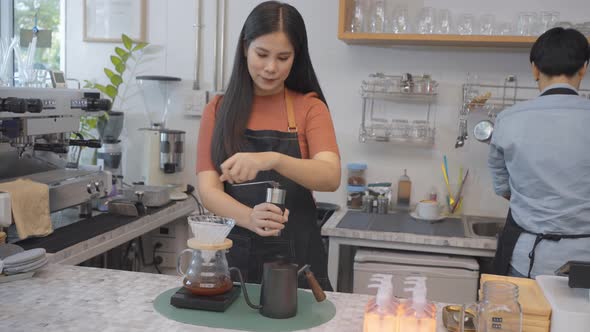 Young woman who is coffee shop business owner uses a manual coffee grinder to grind coffee beans.