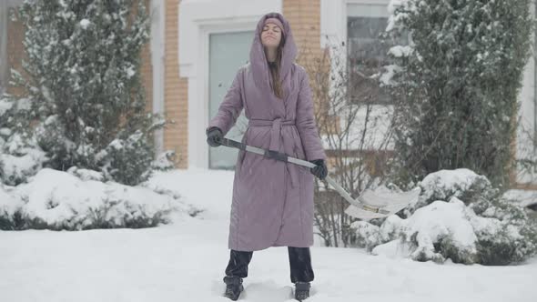 Wide Shot of Positive Smiling Young Woman Standing with Shovel in Snowfall