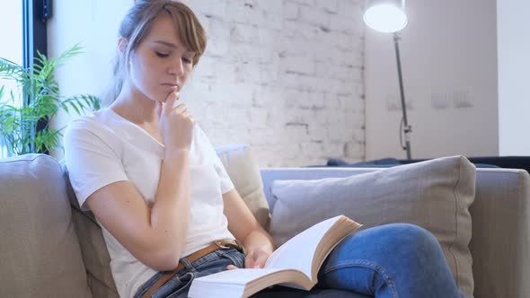 Pensive Woman Reading Book while Sitting on Sofa