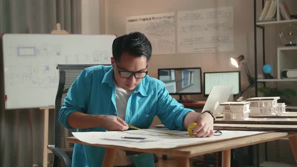 Asian Man Engineer With A Laptop Measuring Blueprint At The Office