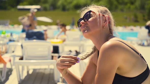 Slow Motion, Close-up: Blonde Girl Is Sitting on Deck Chair, on Beach, in Sunglasses