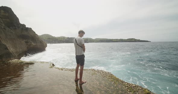 Back View of a White Male Tourist Standing on the Flooded Cliff Beach and Looking Into an Ocean at