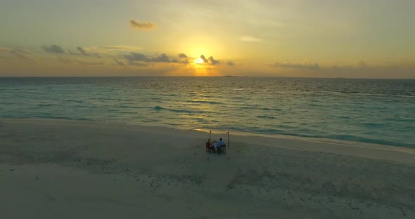 Aerial drone view of a man and woman eating dinner and dining on a tropical island beach.