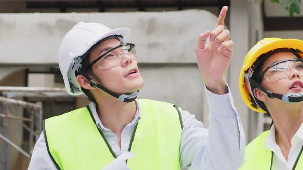 Asian builder workers people wearing safety helmet, holding drawing working on construction side.