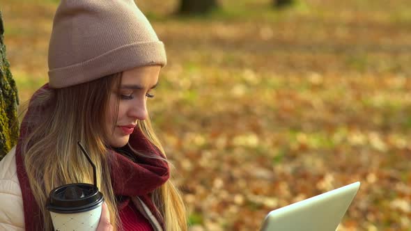 Beautiful Girl, Close-up, Looking at the Laptop Screen. In Autumn Park with Coffee.